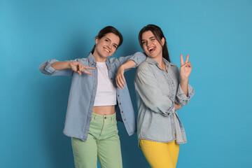 Portrait of beautiful twin sisters showing peace signs on light blue background