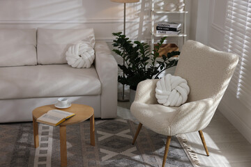 Obraz premium Soft armchair, coffee table, sofa and green houseplant in living room