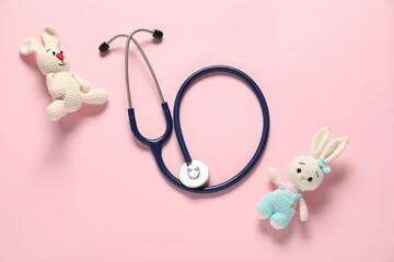 Pediatrics concept. Toy bunnies with stethoscope on pink background, flat lay