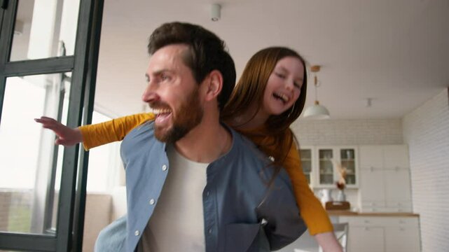 Carefree playful Caucasian daddy man father parent holding daughter little child pretend flying airplane piggyback ride. Male dad kid girl play funny game together fooling around laugh family at home