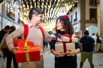 Happy latin couple carrying christmas gifts under city lights