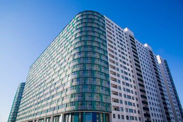 Obraz premium Modern residential high-rise buildings with glass facades and balconies under a clear blue sky, showcasing contemporary architectural design