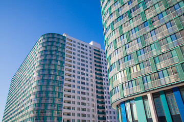 Fototapeta premium Newly constructed modern residential buildings with glass facades and balconies in a contemporary architectural style under a bright blue sky