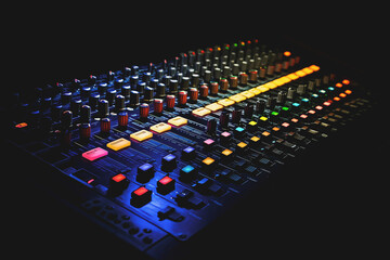 Fototapeta premium Vividly lit sound mixing console with colorful buttons and sliders in the dark. 