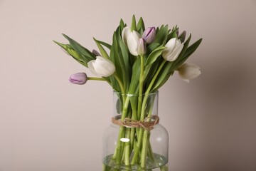 Beautiful bouquet of colorful tulips in glass vase on beige background