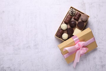 Open box with delicious chocolate candies on white table, top view. Space for text