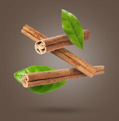 Cinnamon sticks and green leaves in air on greyish brown background