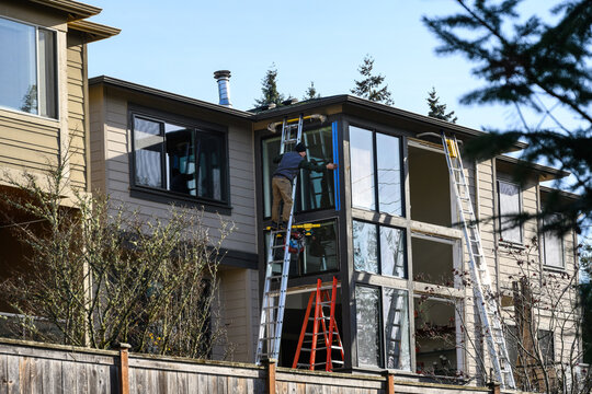 Aluminum extension ladder extended to roof of large two story house, ready for window replacement, outside on a sunny winter day
