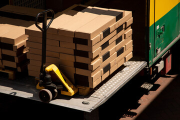 A stack of cardboard boxes on a pallet is being loaded or unloaded from a truck using a yellow pallet jack, representing logistics and transportation © solidmaks
