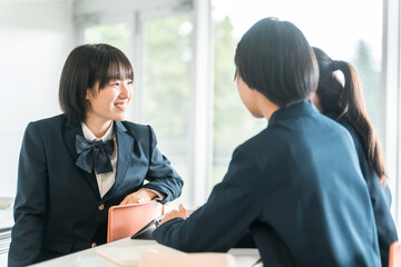 Obraz premium 学校で授業中に後ろの席の生徒と話す小学生・中学生・高校生・女子高生（友達） 