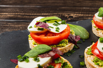 Rice cakes with mozzarella, avocado, spinach, onion on a stone on a wooden table