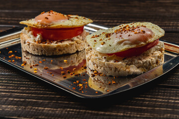 Freshly fried egg on rice bread with tomato and feta cheese on a metal tray
