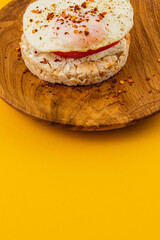 Egg on rice bread with tomato, cheese on a wooden plate on a yellow background