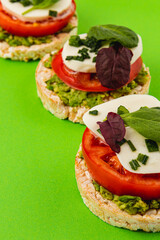 Rice cakes with mozzarella, avocado, spinach and onion on a green background