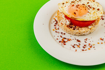 Delicious egg on bread with tomato and cheese on a plate on a green background