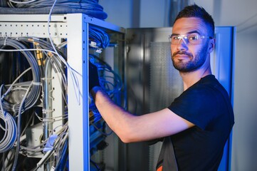 Young man is working with internet equipment and wires in server room