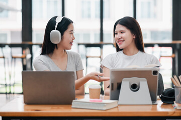 Two young women in a modern office setting, using laptops and tablets, engaged in a lively discussion and collaboration.