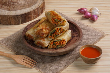 Lumpia or Lunpia, is a traditional snack from central java Indonesia consists of bamboo shoots eggs and meat or shrimp, photographed with wood theme props, studio lighting
