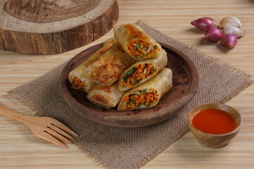 Lumpia or Lunpia, is a traditional snack from central java Indonesia consists of bamboo shoots eggs and meat or shrimp, photographed with wood theme props, studio lighting