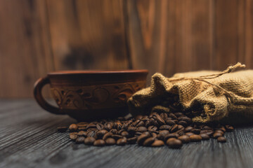 Rustic cup and burlap sack with roasted coffee beans on wooden surface