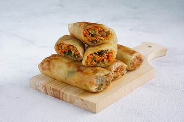 Lumpia or Lunpia, is a traditional snack from central java Indonesia consists of bamboo shoots eggs and meat or shrimp, photographed with wood theme props, studio lighting