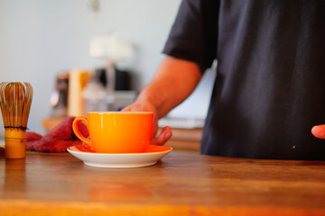 Carefully and intentionally placing a vibrant orange cup on a wooden table