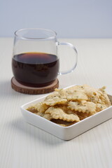 wonton chips in a small white ceramic container on a white table, served with black coffee, with studio lighting