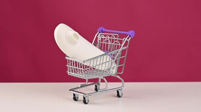 Man putting white vacuum clitoral sex toy into mini shopping cart on pink background. 