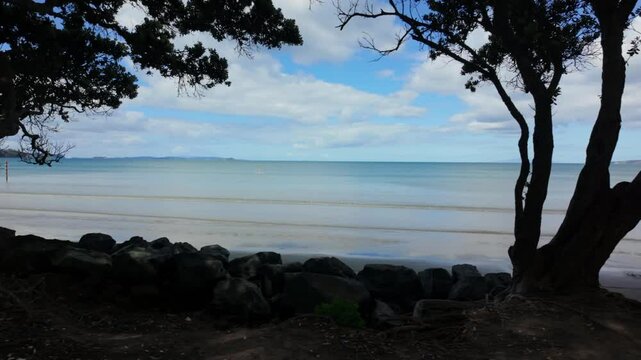 Tranquil beach scene; person paddleboarding in calm ocean; peaceful coastal view. OREWA, AUCKLAND, NEW ZEALAND
