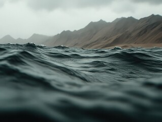 Dramatic View of Turbulent Ocean Waves Under Overcast Skies with Mountainous Landscape in the Background Evoking a Sense of Raw Nature and Wilderness