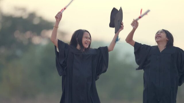 Two women in graduation gowns are holding their caps and gowns in the air. They are smiling and seem happy