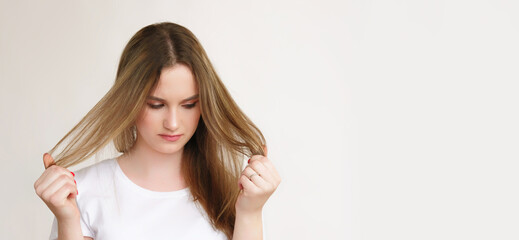 Hair trouble. Vitamin lack. Dissatisfied woman in white t-shirt looking at dry damaged bad ends isolated on light copy space background.