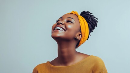A joyful woman wearing a yellow headband and sweater with braided hair and a radiant smile looking up against a clean white background