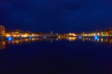 Night view of Marseille harbor showcases vibrant lights reflecting on calm waters