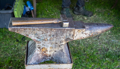 Rustic metal anvil and hammer on grass, representing traditional blacksmithing tools and...