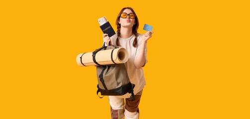 Young female tourist with passport, luggage and credit card on yellow background. Travel concept