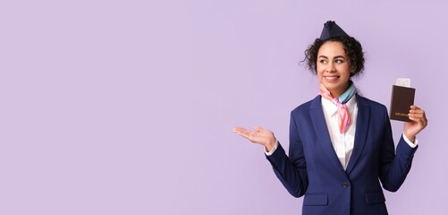 Beautiful African-American stewardess with passport and ticket showing something on lilac background with space for text