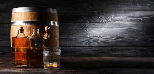 Barrel, bottles and glass of rum on dark wooden background with space for text