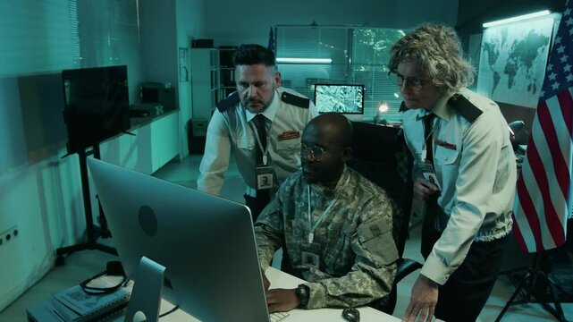Medium zoom-in shot of multiethnic male and female officers in uniform looking at reconnaissance data on computer screen at USA army headquarters, pointing at screen and discussing strategic maneuvers