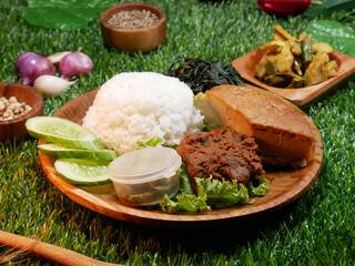 Close up Padang Rice is a complete traditional food from Padang, Indonesia on a wooden plate, containing white rice, beef rendang, omelette, sliced cucumber, green chili sauce and jackfruit vegetable.