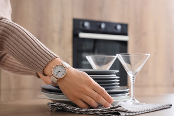 Female hands with stack of plates and glasses on counter in kitchen. Closeup