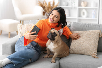 Pretty young woman with french bulldog taking selfie on sofa at home