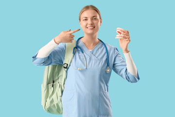Female medical student with jaw model pointing at her teeth on blue background