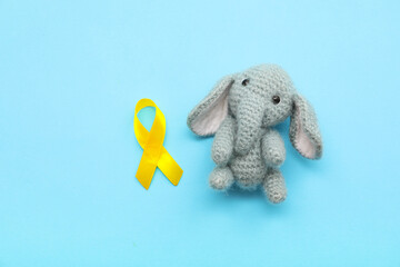Knitted toy elephant and golden awareness ribbon on color background. International Childhood Cancer Day