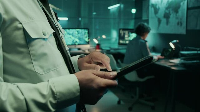 Side closeup of hands and face of Caucasian army commander in uniform shirt with shoulder patches standing in military headquarters office, using tablet computer with satellite data