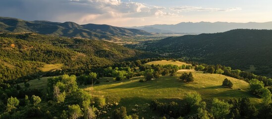 Obraz premium Aerial panorama of serene mountain landscape capturing lush greenery and rolling hills under a vibrant sky with distant peaks in view.
