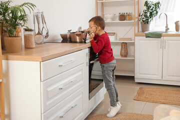 Cute little boy with cooking pot on stove in kitchen. Child at risk