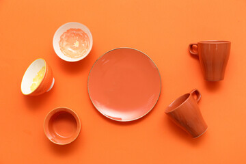 Cups, bowls and plate on orange background