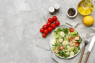 Plate with tasty Caesar salad, lemon, oil and bowl of peppercorn on grey background
