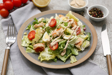 Plate with tasty chicken Caesar salad and bowl of peppercorn on grey background